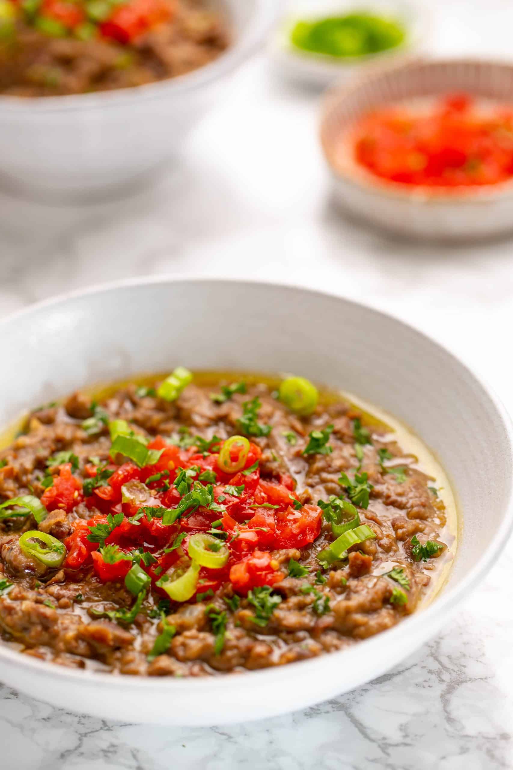 a white bowl of ful Medames topped with tomatoes