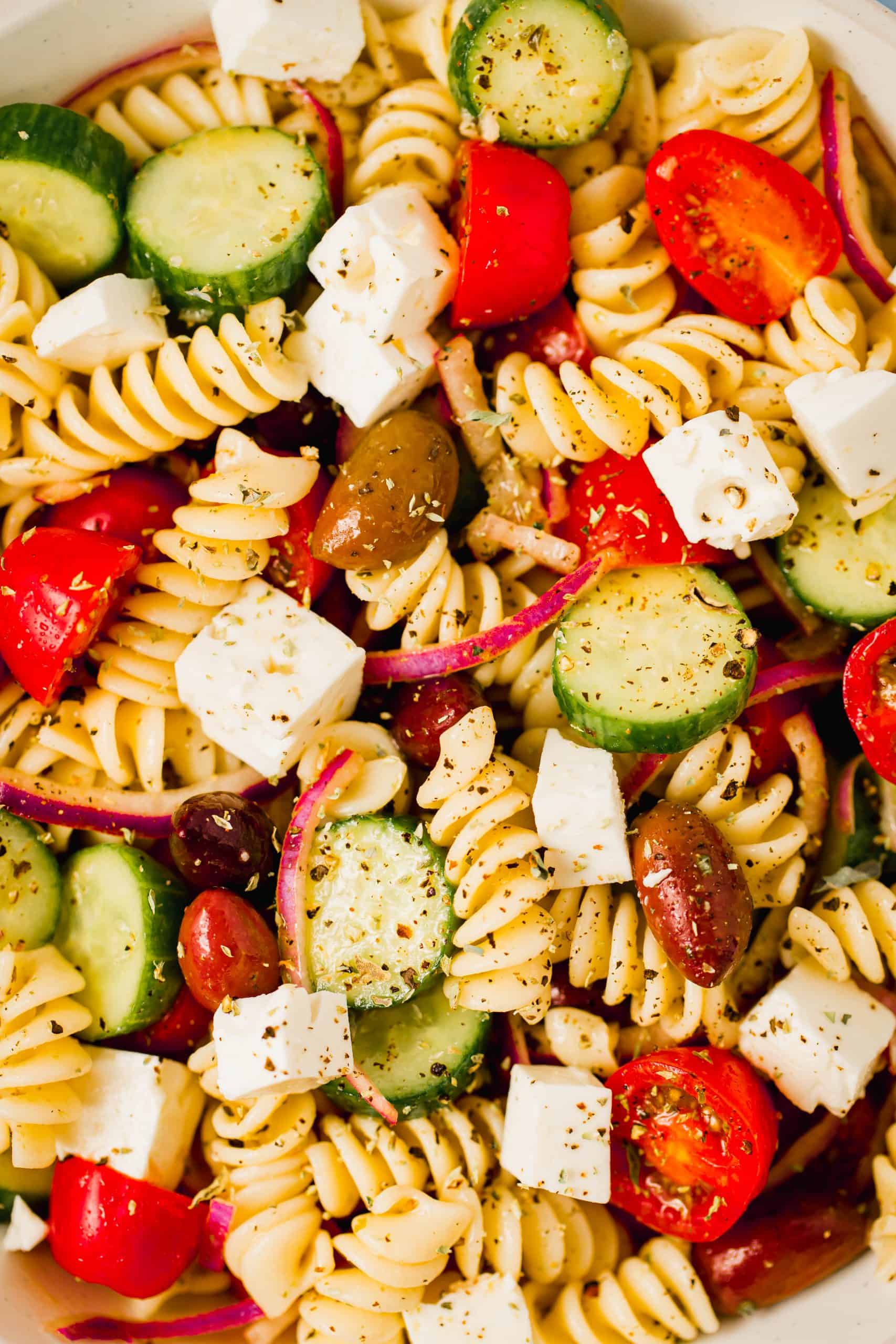 fusilli pasta, cherry tomatoes, cucumbers, feta and red onions in a close up photo