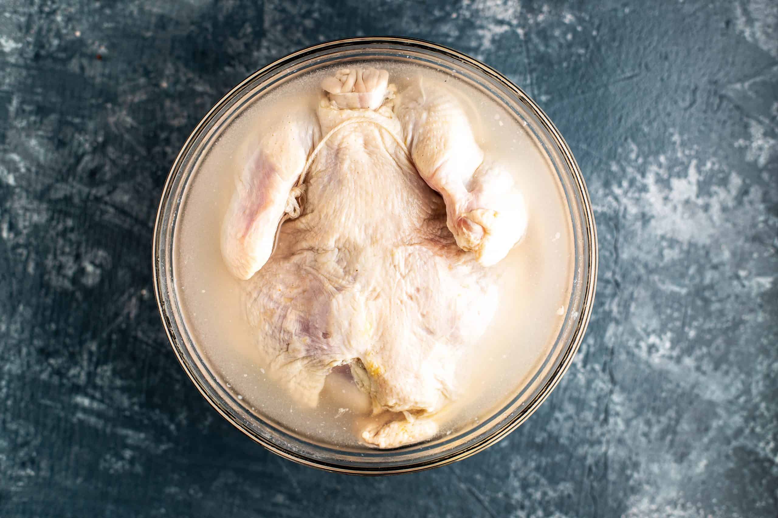 whole chicken in a glass bowl filled with brine