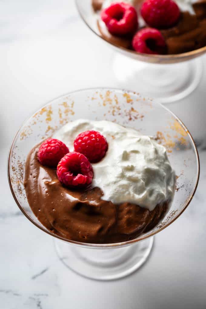 close up of chocolate avocado pudding with raspberries and whip cream