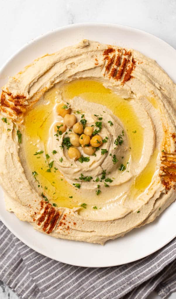 closeup of authentic hummus swirled on a plate with chickpeas, olive oil and paprika