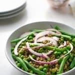 mung beans, green beans, green pea salad with pickled onion in a white bowl, three white plate and two glasses in the back ground