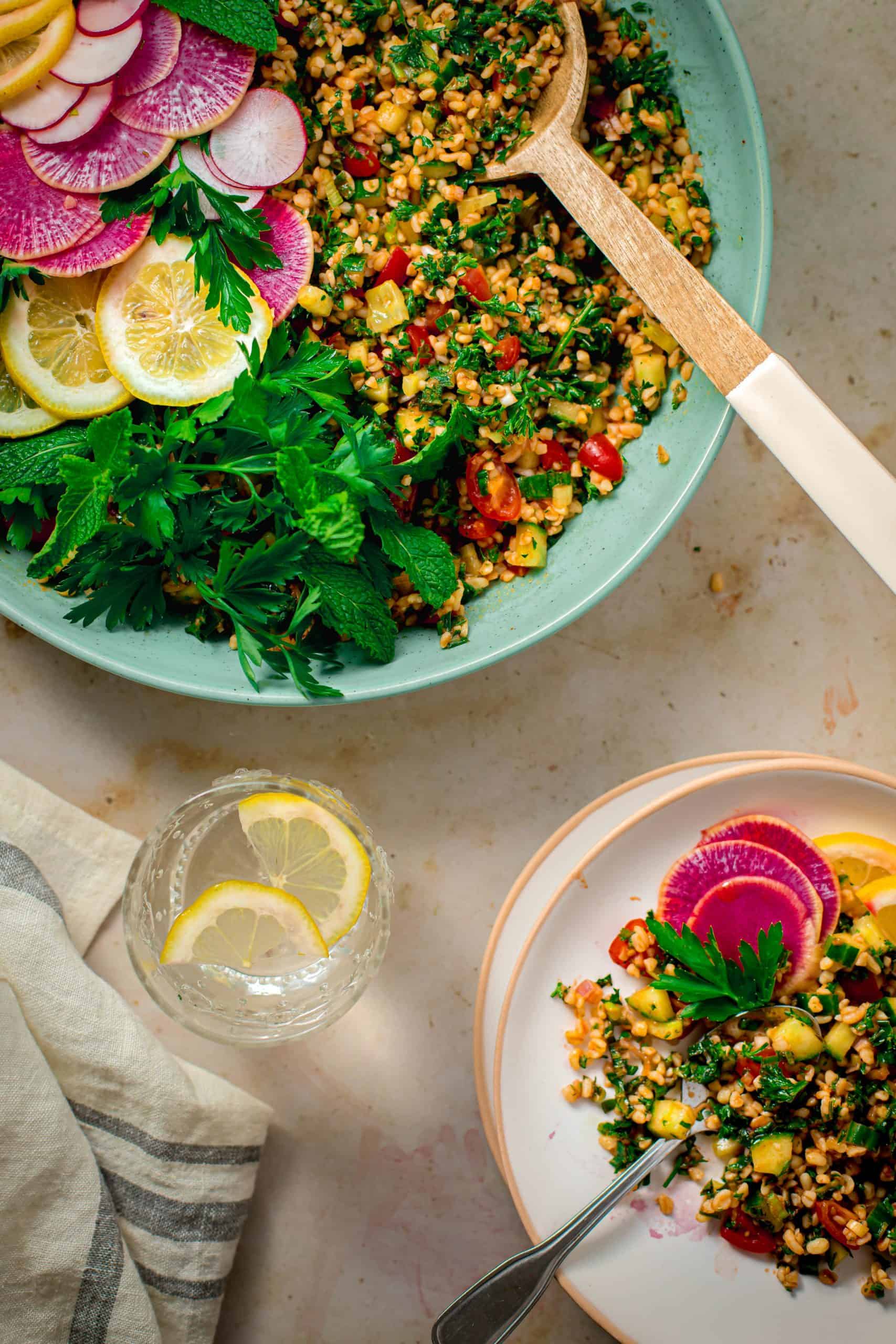 Bulgur salad in a large bowl with a salad spoon and a small plate with salad on it