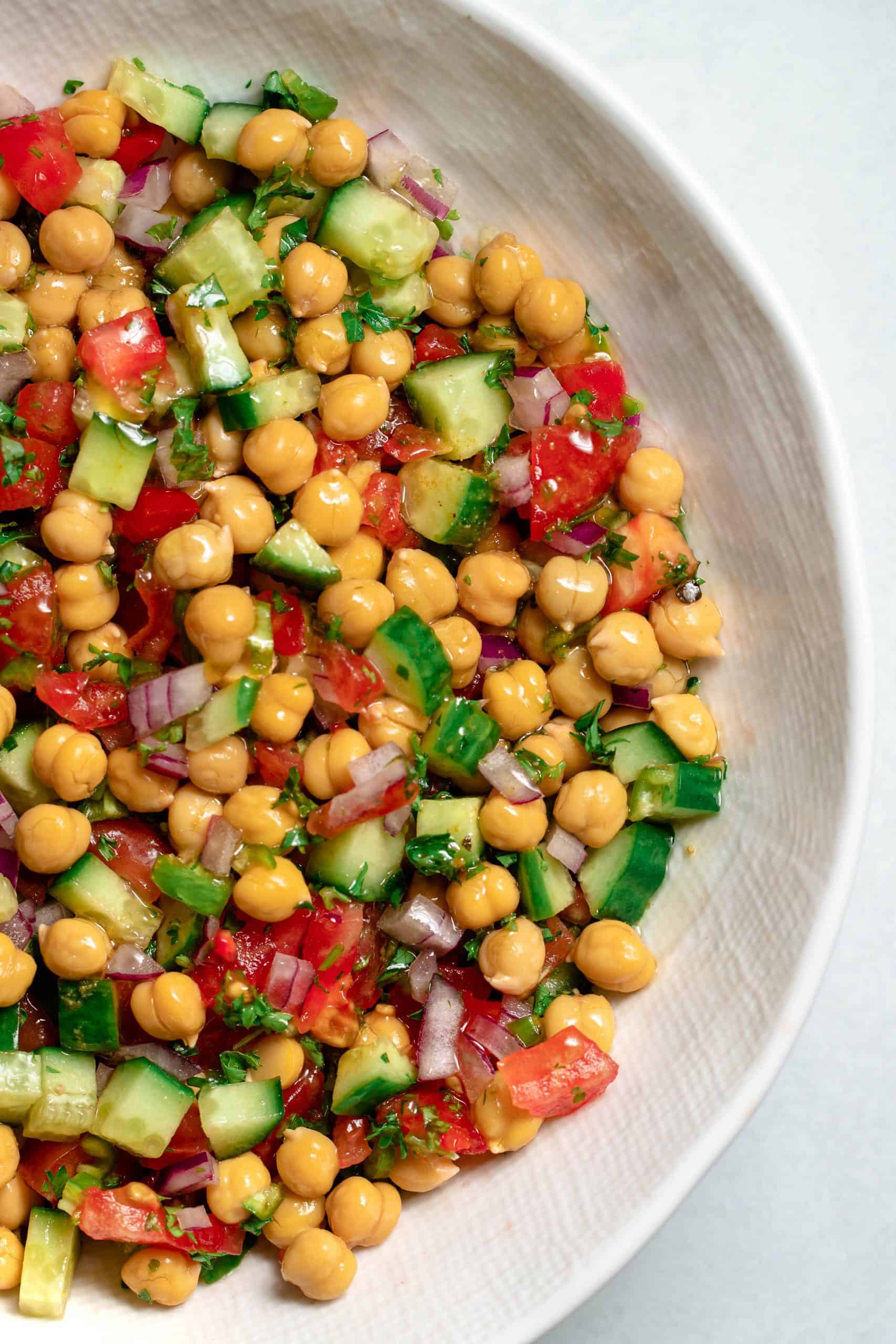 White bowl filled with chickpea, cucumbers, tomatoes, parsley and lemony cumin dressing