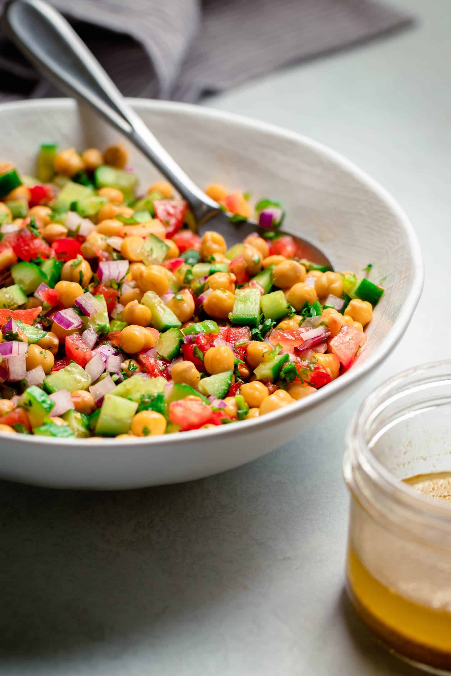 A white bowl of chickpea, tomatoes, cucumbers marinated in a lemony dressing