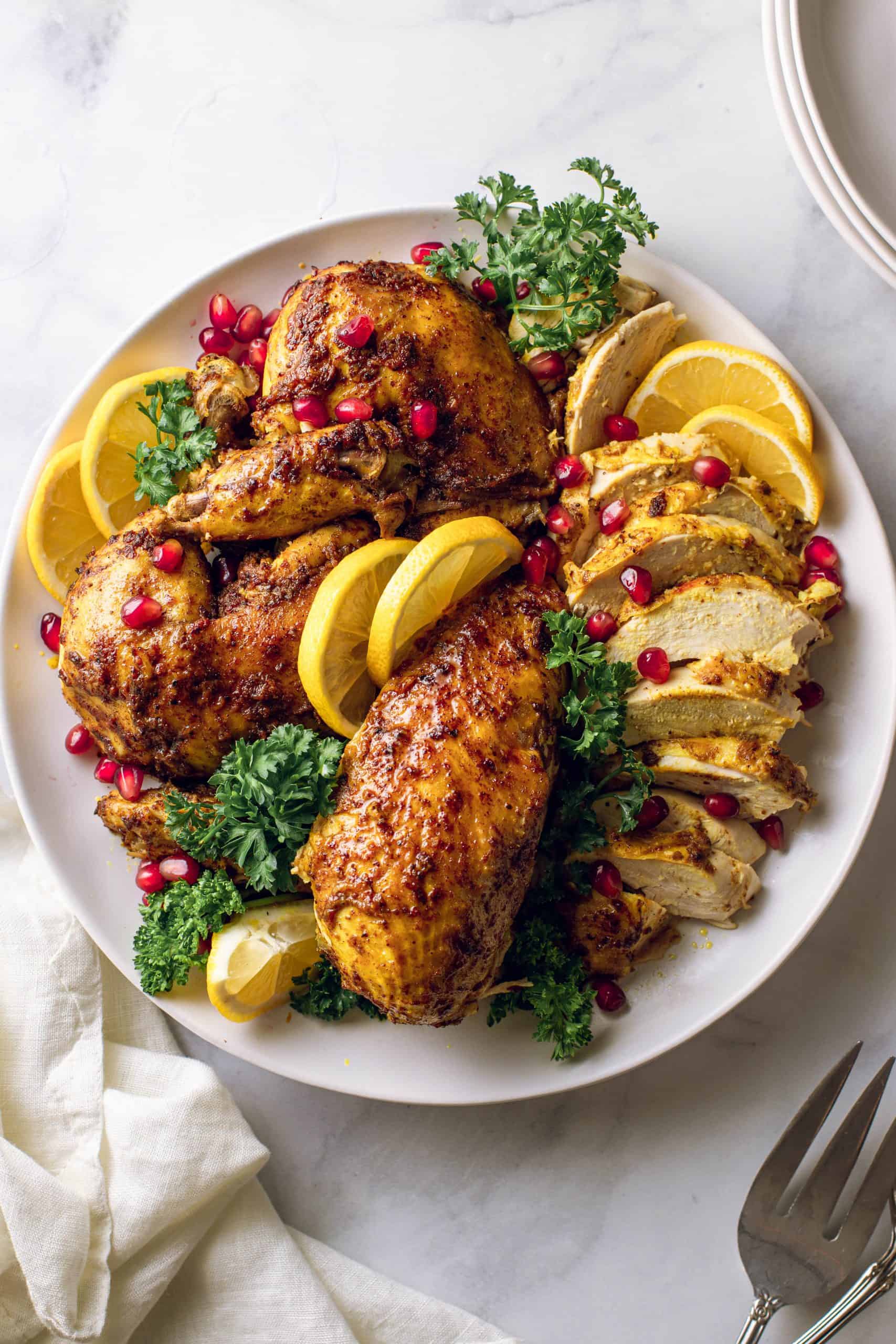 Whole Chicken cut into sections on a white plate with lemons and pomegranate seeds