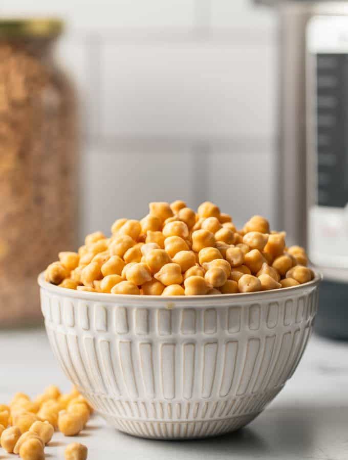 A bowl of uncooked chickpeas on a counter with an instant pot and a jar of dried chickpeas