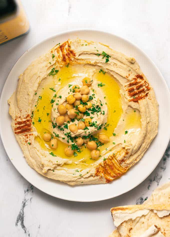 Authentic hummus swirled on a white plate topped with olive oil, chickpeas and paprika