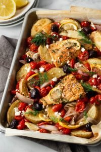 Greek Sheet pan Cod Dinner- A sheet pan filled with cod, roasted potatoes, cherry tomatoes, shallots, black olives and feta