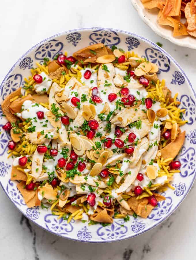 Chicken fatteh in a decorative bowl topped with pomegrantes, almonds, and parsley