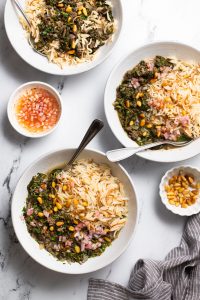 three white bowls of Lebanese spinach stew served with rice and a side of shallot & lemon topping and pine nuts.