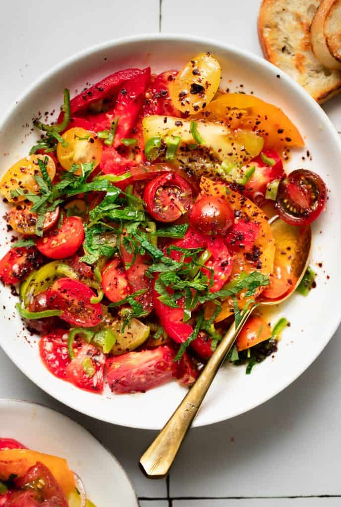 close up of tomato sumac salad in a white bowl with a gold spoon
