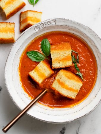 a decorative bowl filled with tomato soup and three brioche grilled cheese croutons